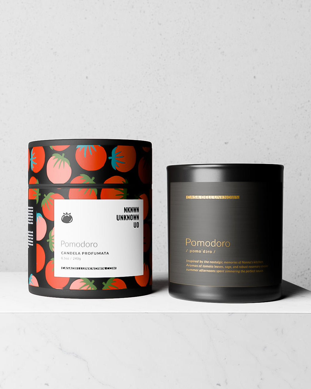 Two candles, one with a tomato pattern and the other plain black, on a white surface.