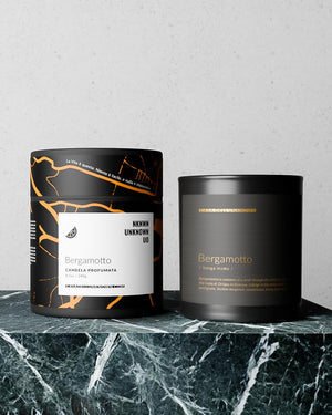 Two black candles with labels on a marble surface against a light gray background