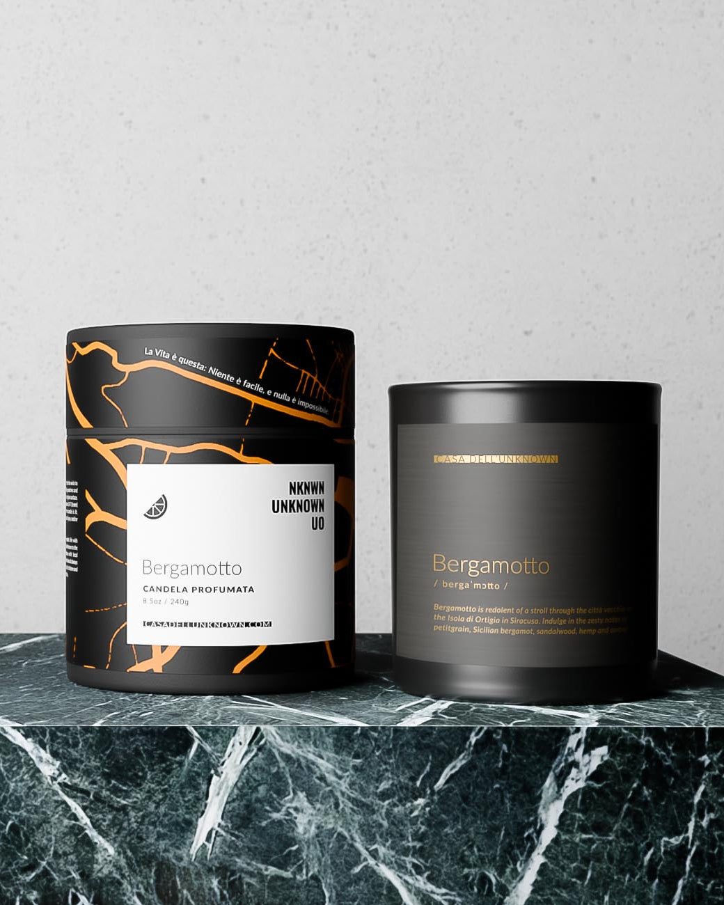 Two black candles with labels on a marble surface against a light gray background