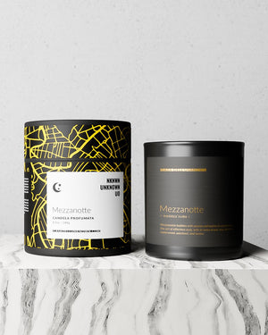 Two scented candles from the brand Mezzanoite are displayed on a white marble surface against a light gray textured wall. The candle on the left is in a black tin with a yellow street-map pattern and a white label.