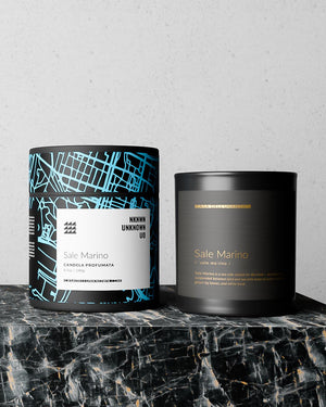 Two candles from the brand Casa dell' Unknown named 'Sale Marino', displayed on a black marble surface against a light gray textured wall.